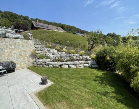 Jardin aménagé avec un mur en pierres, une terrasse et une pelouse
