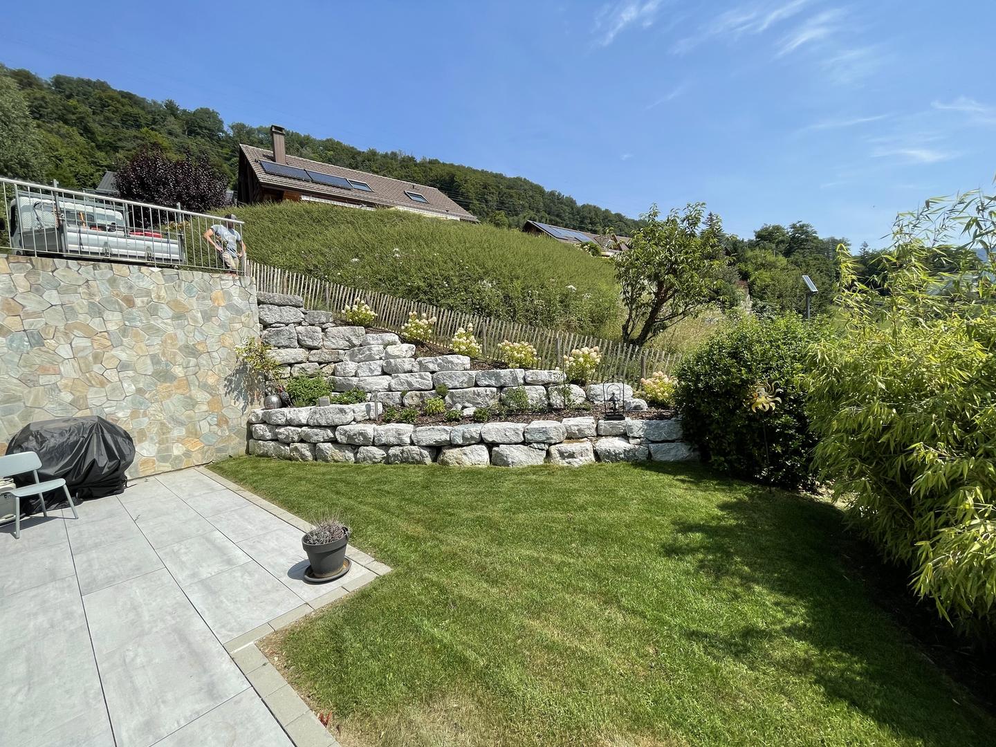 Jardin aménagé avec un mur en pierres, une terrasse et une pelouse